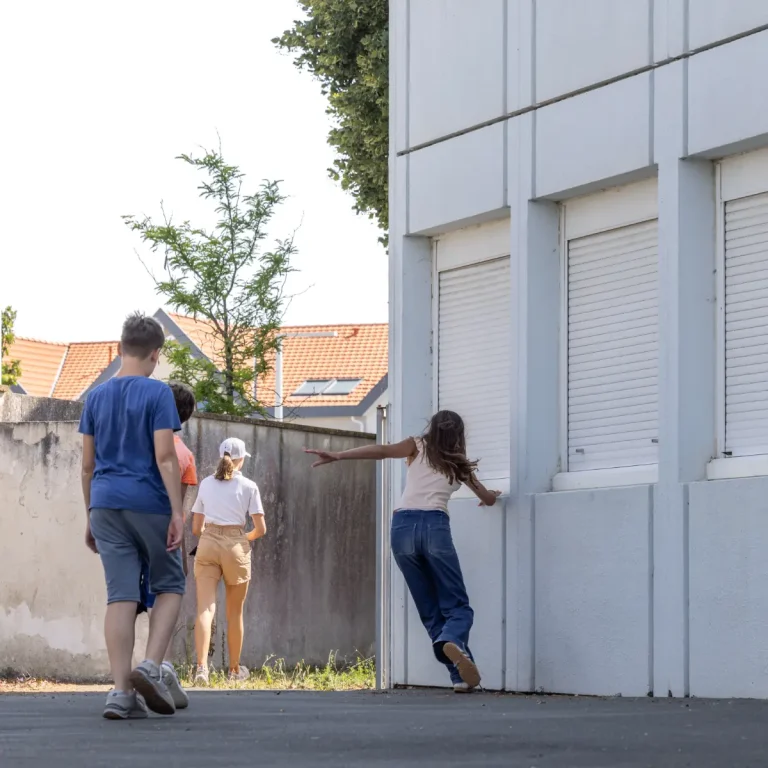 Trois jeunes gens de dos, dansent en contournant un bâtiment.